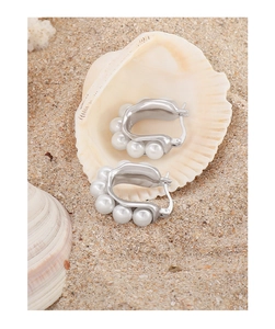 Detail of silver U-shaped earrings with white pearls nestled in a seashell on a beach