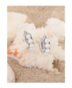 Macro shot of silver U-shaped pea pod earrings with pearls on white coral and beach sand