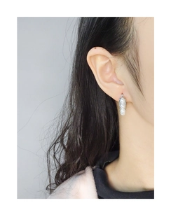 Detailed close-up of U-shaped silver earrings with three vertical pearls on an ear