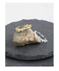 Macro shot of silver and gold vine branch rings with zircons on dark natural rocks
