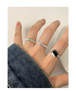 Détail de bagues en argent avec pierres vertes, roses et noires portées à la main
