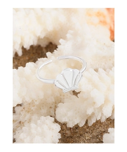 Macro detail of silver shell ring on white coral background with sandy texture