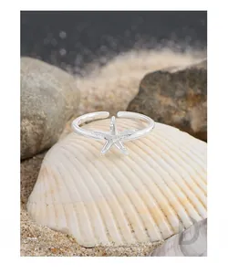 Macro detail of silver starfish ring on white shell with beach sand background