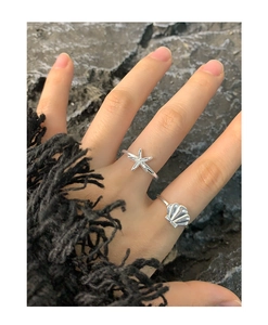 Detail of S925 silver starfish and seashell rings worn on hand against black rock