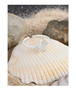 Detail of S925 silver starfish ring placed on a seashell with a beach sand background