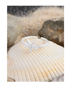 Detailed view of silver starfish ring on a seashell and white sand background