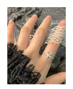 Silver starfish ring on female finger with white lace over a dark grey backdrop