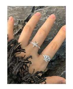 Detailed view of silver S925 starfish and seashell open rings on finger with rock background