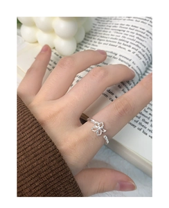 Detail view of the silver hollow flower ring worn on finger with artistic backdrop
