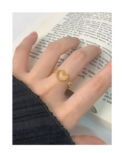 Detailed close-up of a hollow heart-shaped gold ring with beaded edges worn on finger