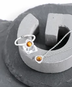 Detailaufnahme von Tigerauge-Halskette und offenem Ring mit faltiger Silberstruktur