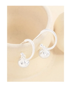Detail view of silver lucky bag drop earrings on a minimalist beige ceramic edge