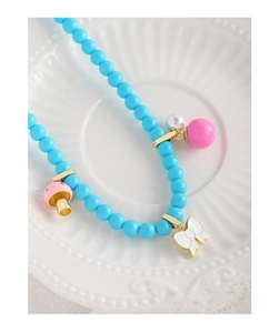Détail du collier de perles bleu clair avec nœud blanc et breloques champignon rose