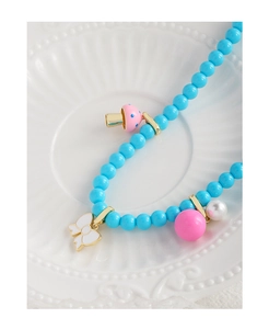 Vue détaillée du collier de perles avec breloques champignon et nœud sur plat céramique
