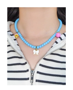 Détail du collier de perles bleues avec nœud blanc, sphère rose et grelot doré