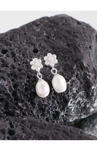 Vue macro de boucles d'oreilles fleur et perle sur une roche volcanique noire