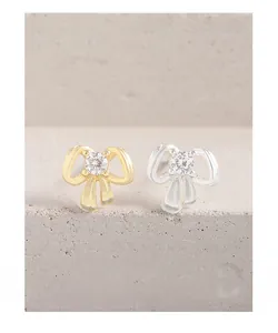 Detailed close-up of two mini bow knot stud earrings in gold and silver plating