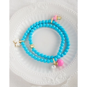 Collier de perles bleu vif avec breloques nœud et champignon sur un plateau en céramique
