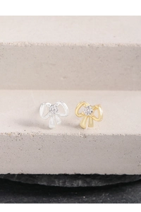 Macro shot of silver and gold bow earrings with central cubic zirconia on a gray podium