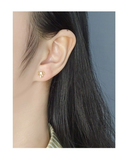 Close-up of a delicate golden bow stud earring with a central zircon on a model's ear