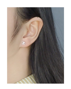 Close-up of small silver bow stud earrings with zircon stone worn on a female earlobe