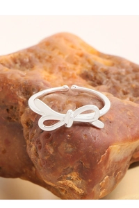 Close-up of a silver bow ring with adjustable opening displayed on a natural red stone