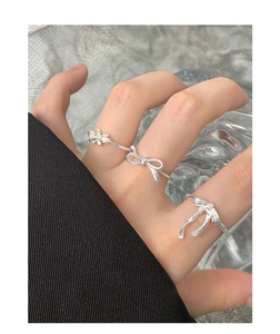 Detailed view of three-piece silver bow and flower rings on a model's finger
