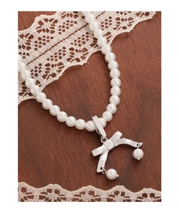 Dettaglio di un ciondolo a fiocco d'argento su una collana di perle bianche su legno