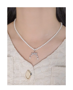 Dettaglio della collana di perle con ciondolo a fiocco argento su modella in tweed