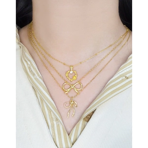 Collier doré à trois rangs avec pendentifs nœud et cœur porté pour un style superposé