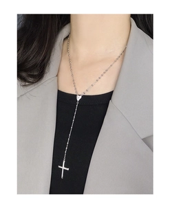 Collier en Y argenté avec pendentif croix et fermoir coeur porté sur un blazer gris