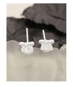 Macro shot of S925 sterling silver bow earrings with round white pearls on glass surface