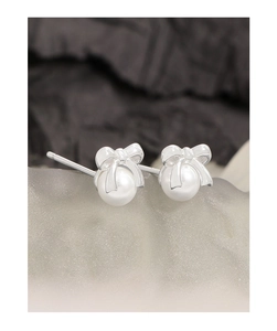 Macro view of S925 silver bowknot earrings with white pearls on a textured stone surface