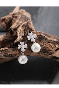 Detail of four-leaf clover pearl earrings with micro-set zircon on rustic wood backdrop