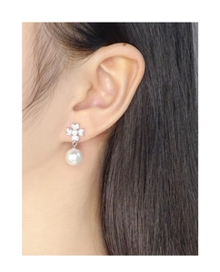Detailed close-up of leaf-shaped zircon flower and elegant white pearl earring on ear