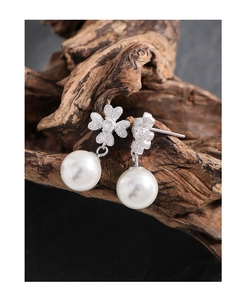 Macro view of clover leaf zirconia studs and elegant hanging white pearls on wood