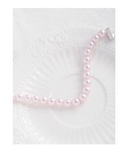 Détail d'un bracelet de perles roses avec fermoir argenté sur fond blanc texturé élégant