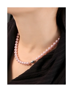 Close-up of elegant pink pearl necklace with silver clasp worn on a black textured garment