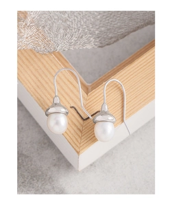 Detailed close-up of acorn-shaped natural pearl earrings on a light wooden frame