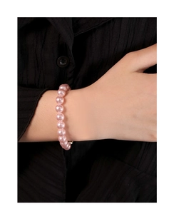 Vue détaillée d'un bracelet en perles roses au poignet sur un tissu plissé noir