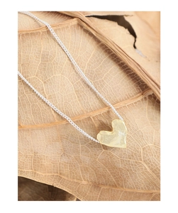 Macro shot of textured gold heart pendant on silver chain over an autumn leaf