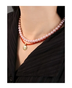 Close-up of double-layer necklace with pink pearls, red beads and golden M pendant