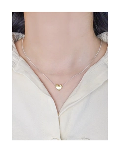 Detail of a gold lava textured heart pendant on a silver chain worn by a model