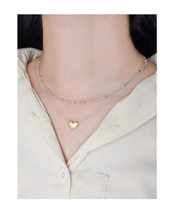 Close-up of layered S925 silver beaded chain with a golden heart pendant on a model