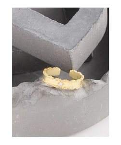 Detail of gold-plated leaf texture ring with sparkling zircon stone on a gray pedestal