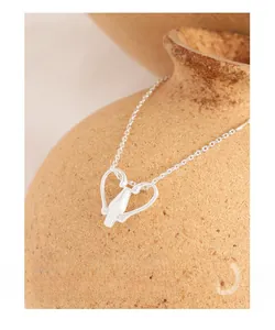 Detail of S925 silver necklace with minimalist heart pendant on a ceramic vase