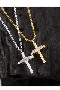 Macro shot of silver and gold twisted cross pendants with zircon inlay on black wood background