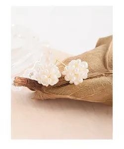 Detailed close-up of clustered white pearl stud earrings on a natural autumn leaf background