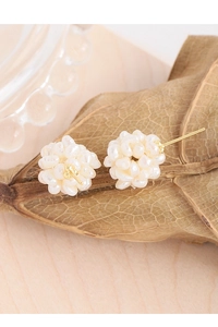 Detail shot of handcrafted pearl firework ball earrings on textured autumn leaves