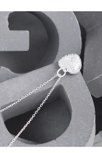 Macro shot of silver heart pendant featuring vintage floral texture and zircon stone